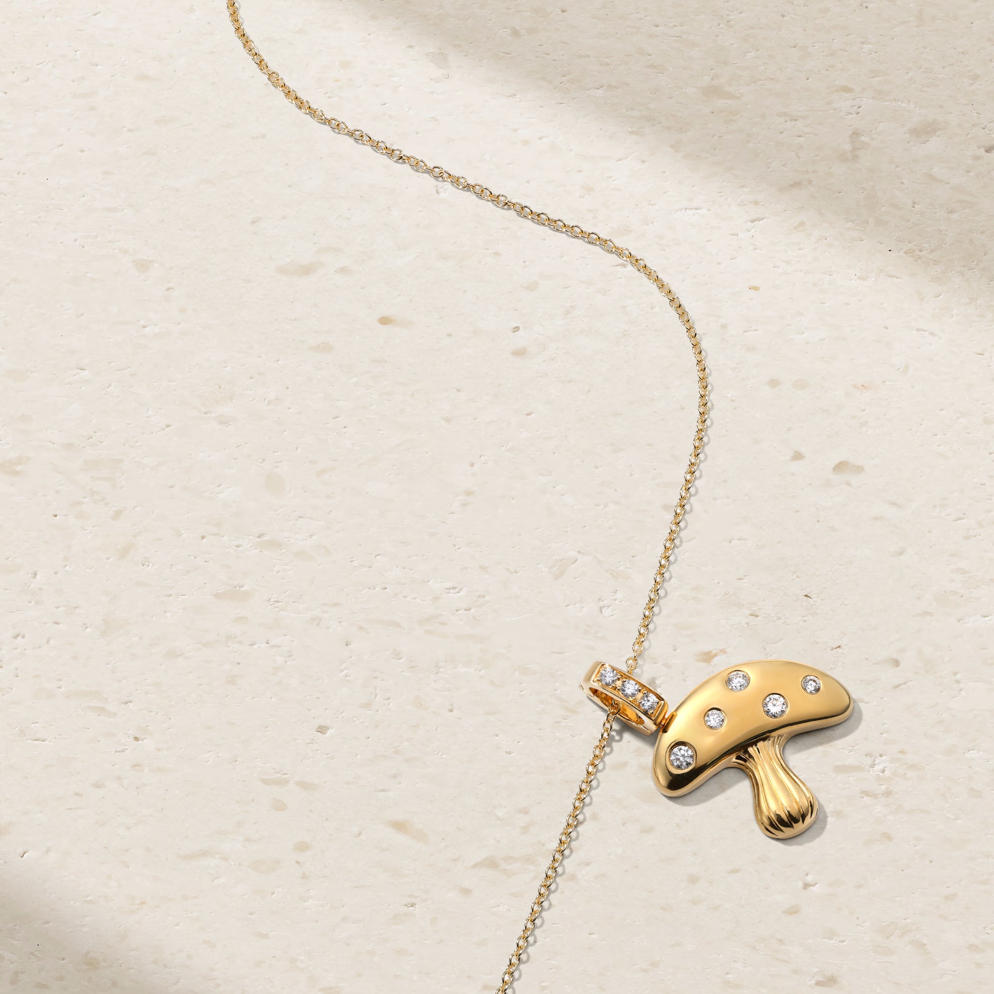 Gold necklace with a mushroom-shaped pendant on a beige background