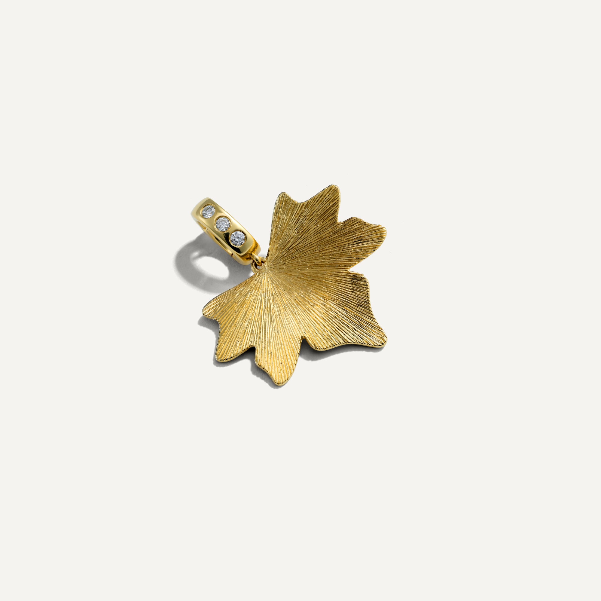 Gold leaf-shaped pendant with embedded stones on a white background