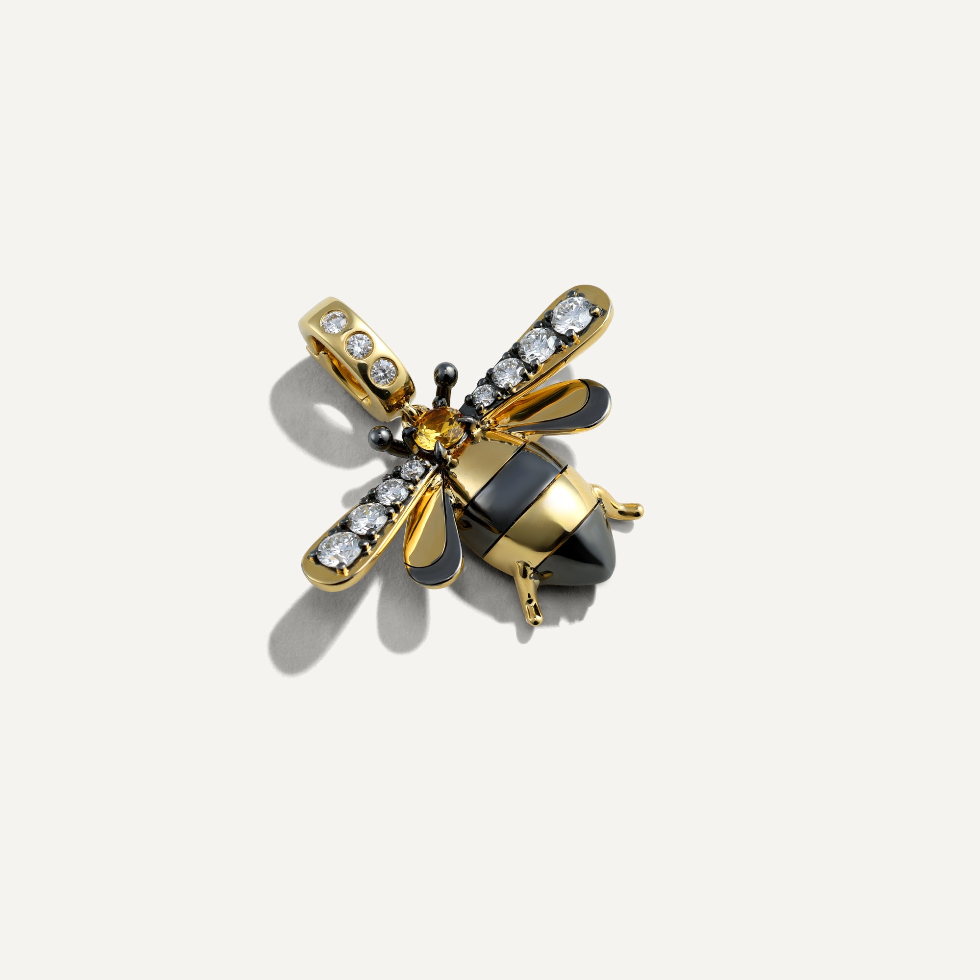 Gold and black bee-shaped pendant with gemstones on a white background